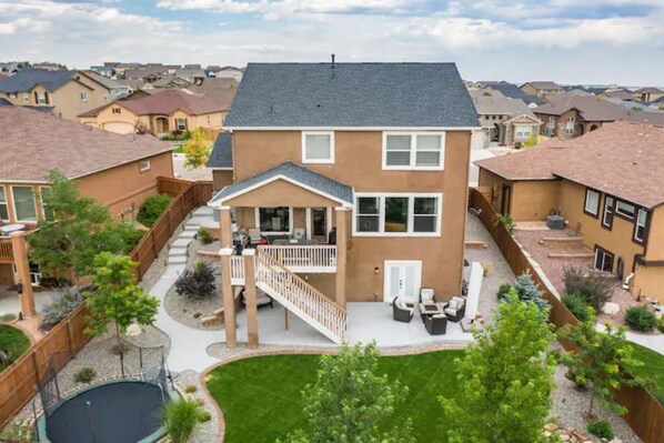 A two-story house with a covered patio, a fenced backyard, and a trampoline.