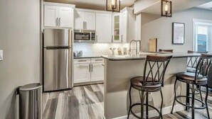 A modern kitchen with stainless steel appliances, white cabinetry, and a bar area with stools.