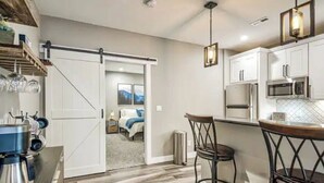 A modern kitchen with white cabinets, a coffee machine, and a sliding door leading to a bedroom.