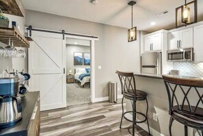 Kitchen features a large sliding door, bar area with stools, microwave and oven, and wooden flooring.
