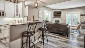 A modern kitchen with white cabinets, a bar area, and a grey sofa in the living area.