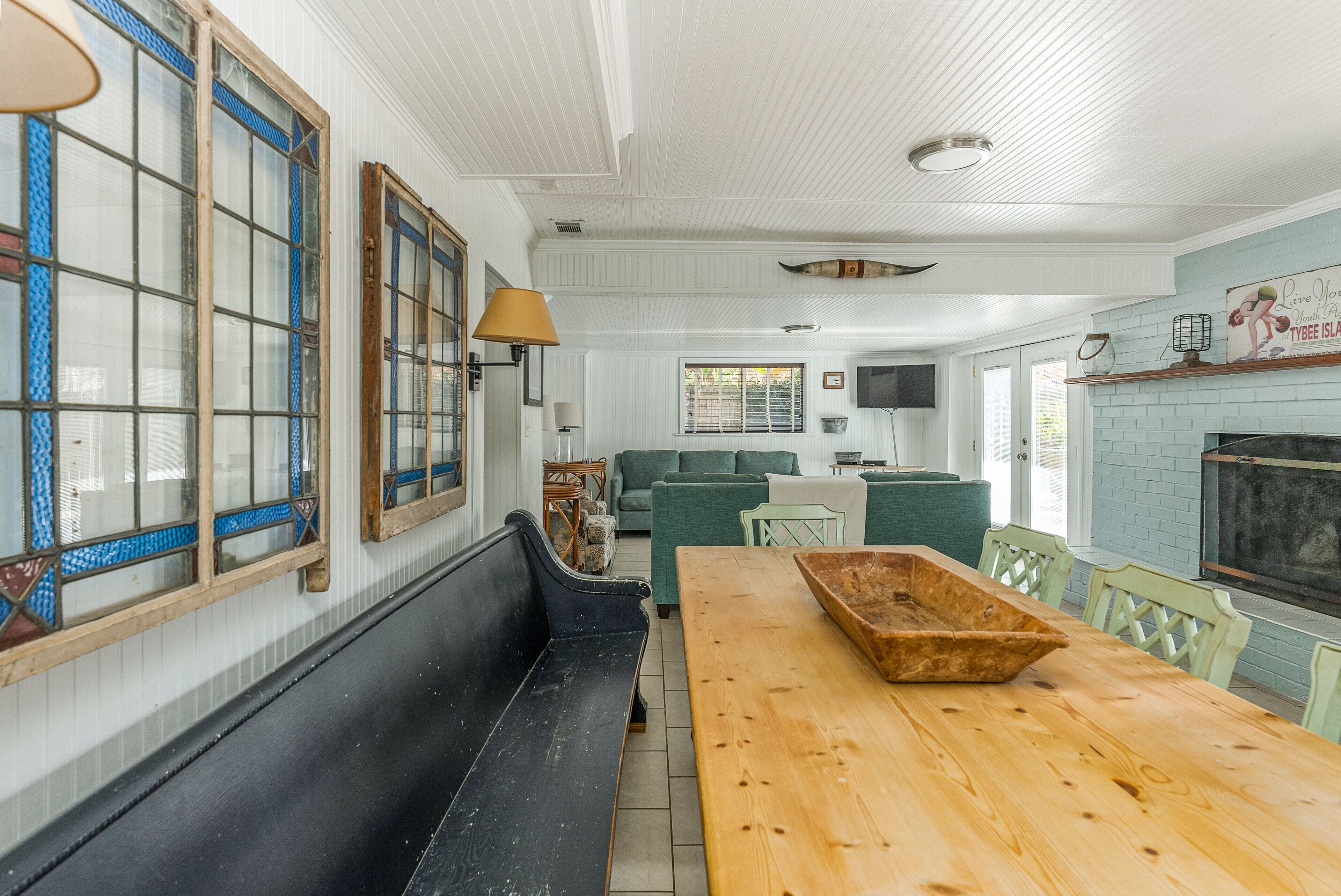 A room with a wooden table, a black bench, green sofas, and a fireplace.