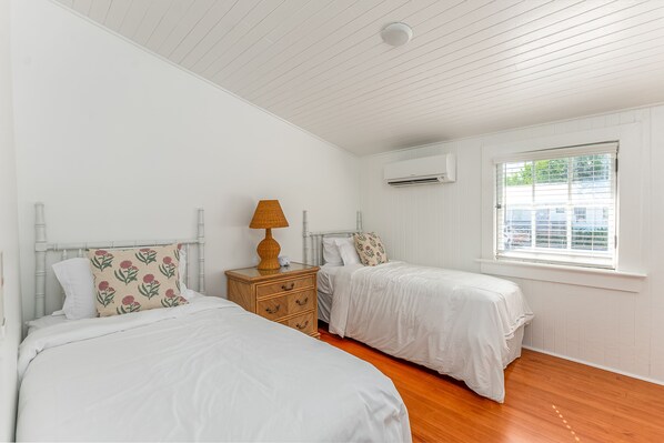 A bedroom with two beds, a wooden nightstand, a lamp, and an air conditioning unit.
