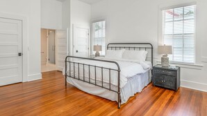 Ein Schlafzimmer mit einem Metallbettgestell, weißer Bettwäsche, einem Nachttisch mit Lampe und einem Fenster mit Jalousien.