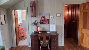 Un bureau en bois avec des tiroirs, une chaise, une décoration murale en macramé, un globe terrestre, une carte encadrée et une petite plante.