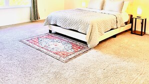 Une chambre à coucher avec un lit, un ventilateur de plafond, une table de chevet avec une lampe, une fenêtre avec des rideaux et un tableau encadré accroché au mur.