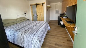 A compact room with a bed, a kitchenette, and a wooden door. - The Sage Motel (Saratoga)