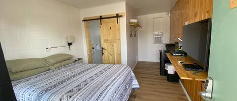 A compact room with a bed, a kitchenette, and a wooden door.