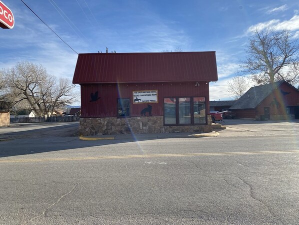 A red building with a stone base, a sign advertising a clean and comfortable room, and a parking lot in front.