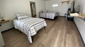 A bedroom with two beds, a desk, a chair, and a TV. - The Sage Motel (Saratoga)