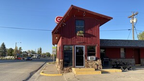 A red building with a 'C' logo, a stone base, and a 'SCHOOL SPEED LIMIT 20' sign. - The Sage Motel (Saratoga)