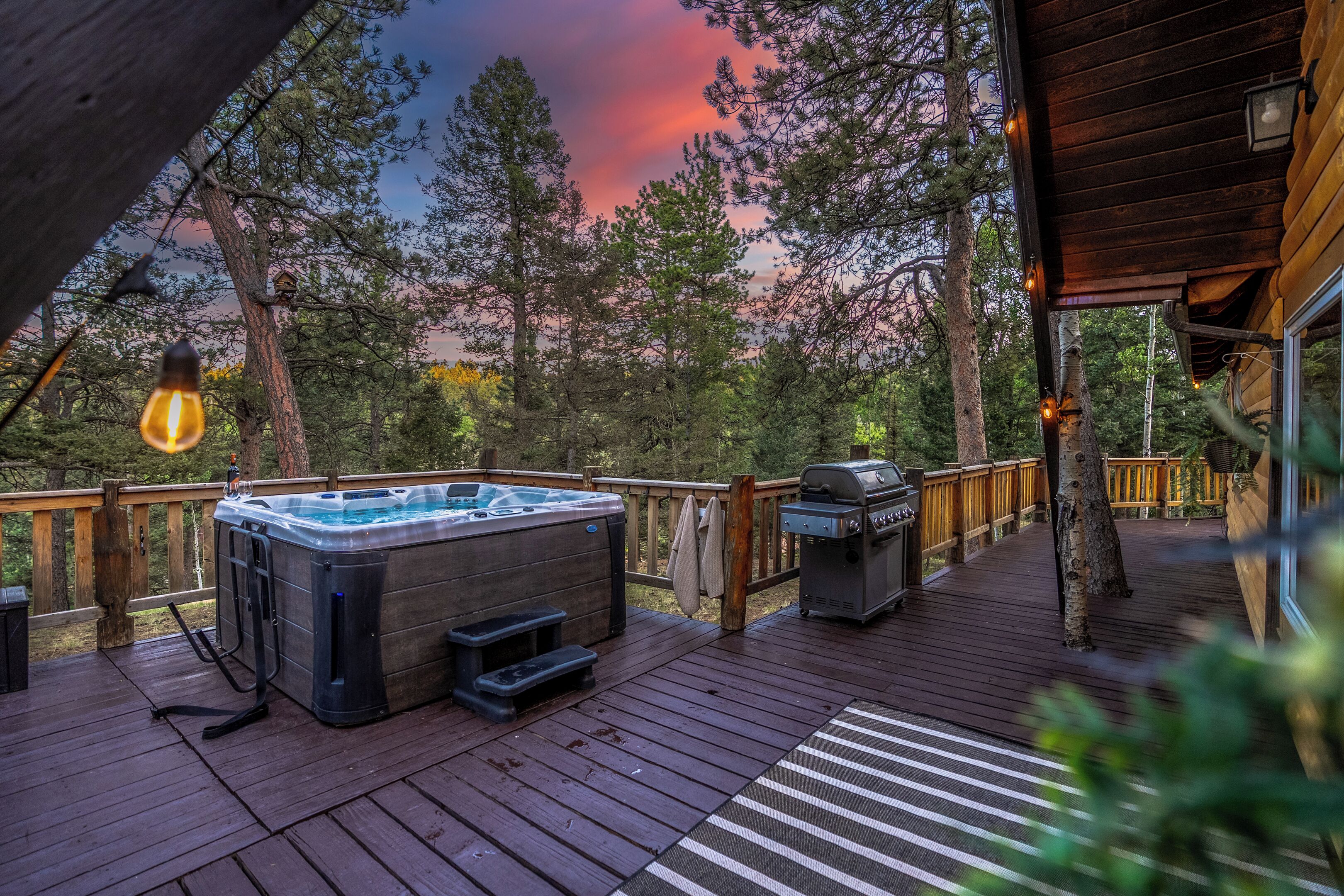 Une terrasse en bois avec un jacuzzi, un barbecue et des guirlandes lumineuses.