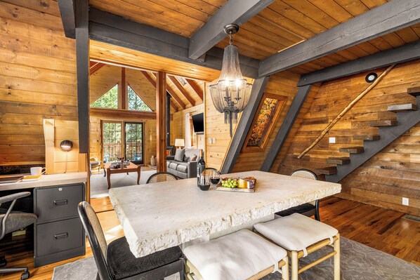 A wooden interior with a dining table, chairs, a chandelier, and a staircase. - Secluded Mountain A-Frame: Hot Tub, BBQ, & Large Deck, by Forest & Peak Retreats (Divide)