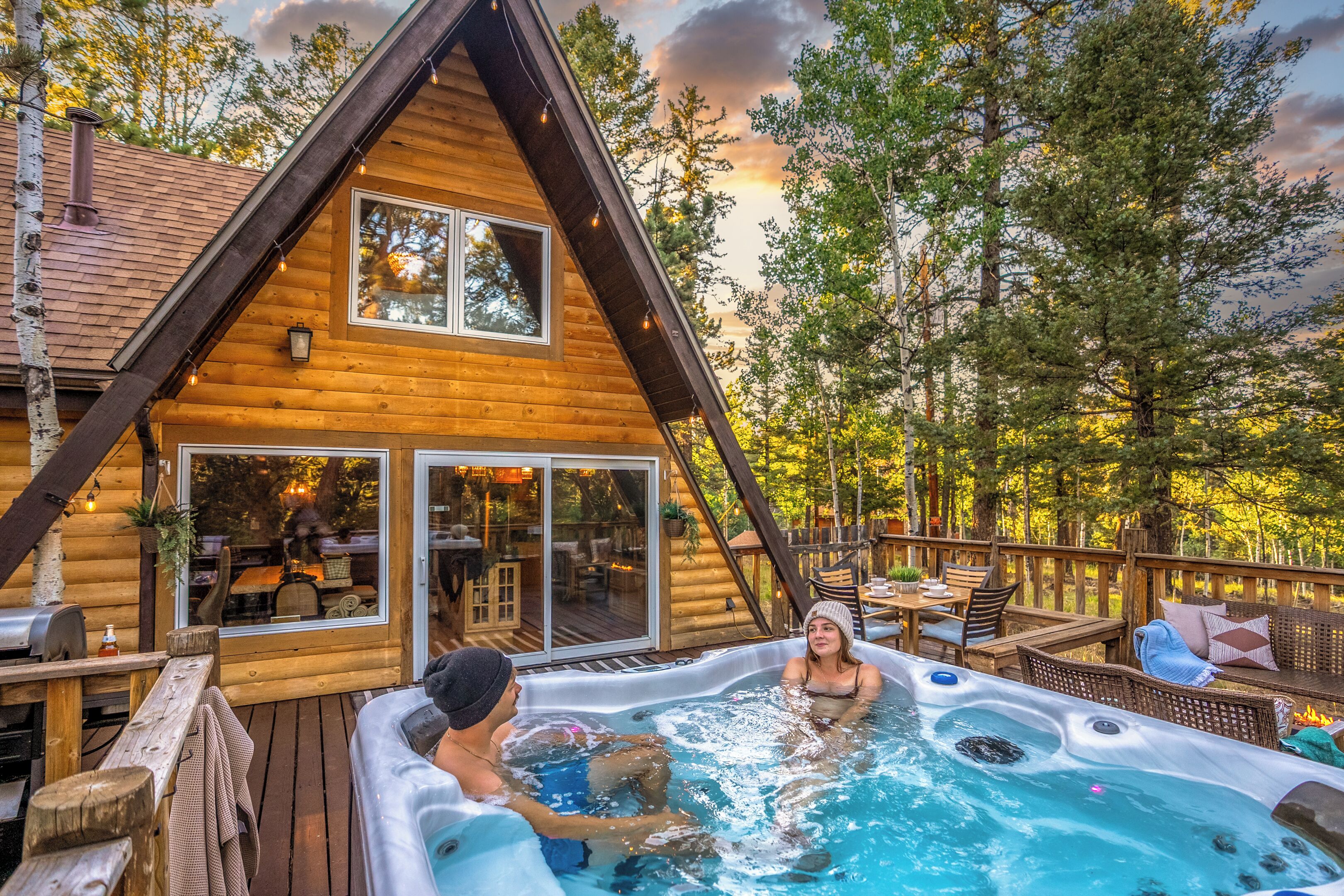 Una cabaña con jacuzzi, terraza de madera y vistas al bosque circundante.