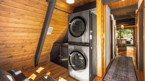 A laundry room with two stacked front-loading washers and dryers, wooden walls, and a visible exit door.
