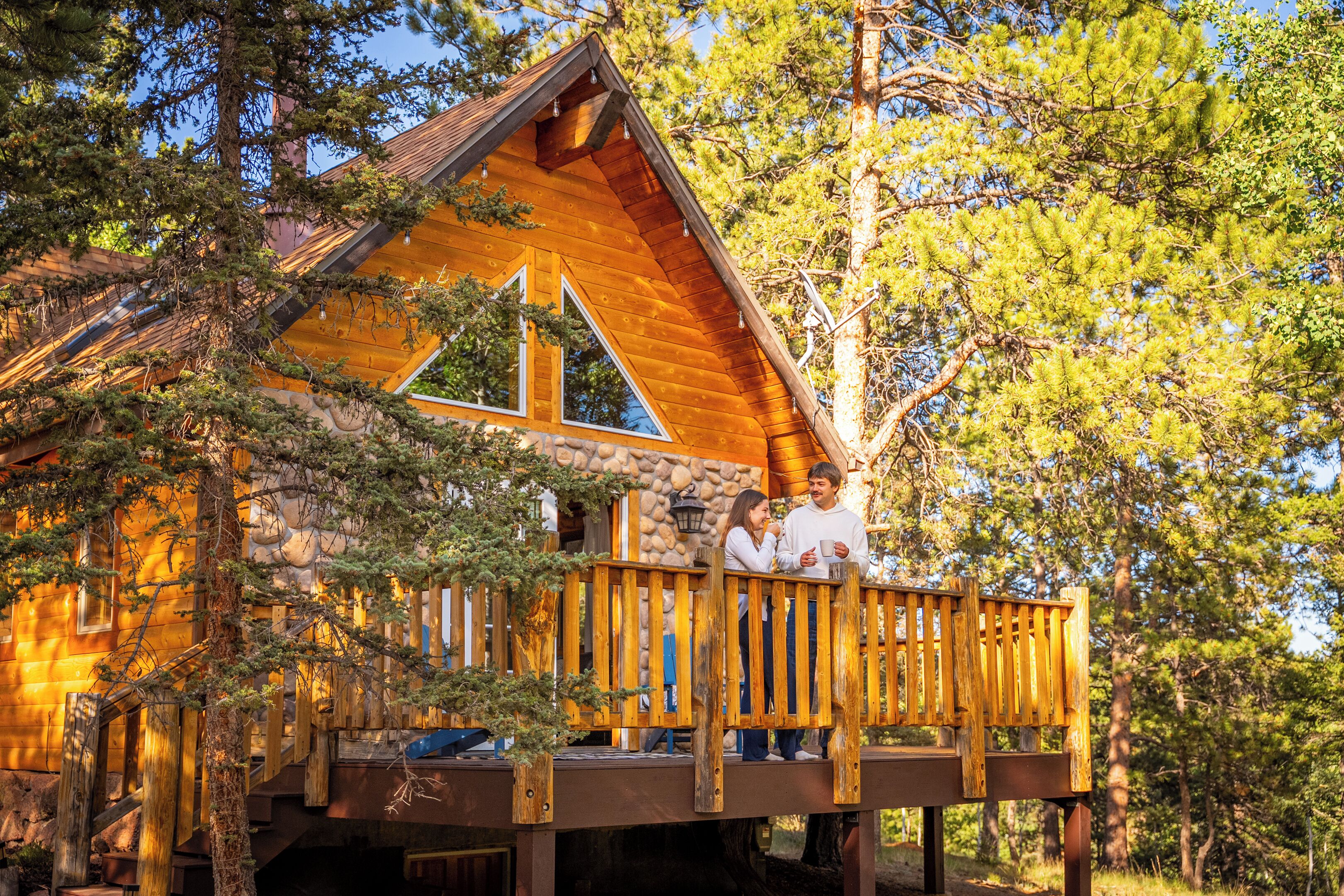 A cabin with a wooden deck, stone walls, and a large window.