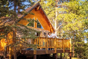 A cabin with a wooden deck, stone walls, and a large window. - Secluded Mountain A-Frame: Hot Tub, BBQ, & Large Deck, by Forest & Peak Retreats (Divide)