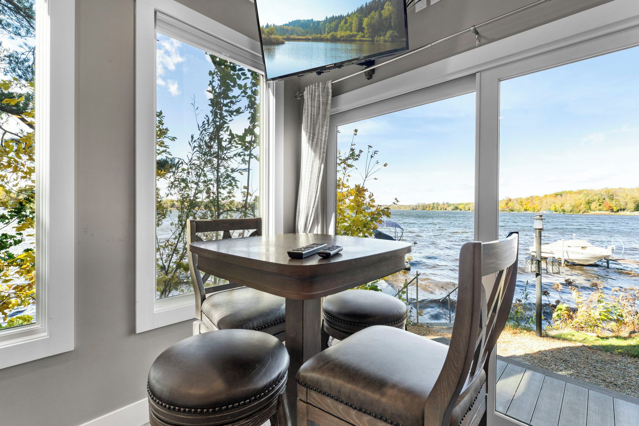 A room with a table and chairs, a television, and a view of a lake.