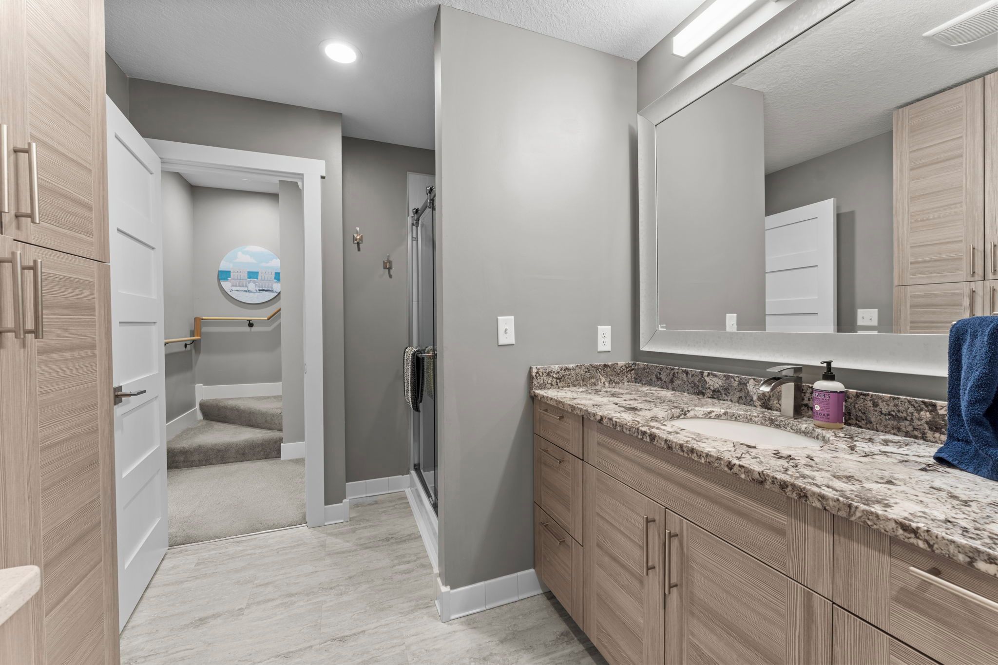 A modern bathroom with a shower, a sink with a granite countertop, and a large mirror.