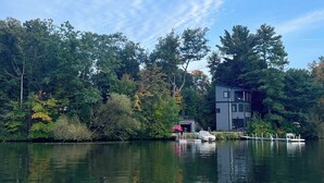 A lakeside property with a dock, a small boat, and a building surrounded by trees. - Lakefront Luxury Modern Home With Docks, Fire Pit & Pontoon Boat Rental (Turtle Lake)