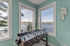 Quarto com mesa de futebol, janelas amplas com vista para um lago e decoração de cavalo-marinho na parede.