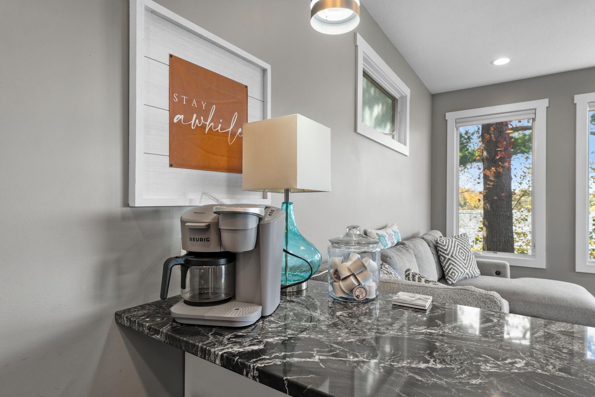 Una cocina moderna con cafetera, lámpara y ventana con hojas otoñales.
