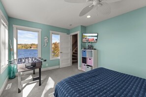 Quarto com cama, mesa de pebolim, televisão e vista para um lago.