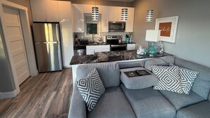 A modern kitchen with a refrigerator, microwave, and stove. There is a gray sofa with patterned cushions and a small table. - Lakefront Luxury Modern Home With Docks, Fire Pit & Pontoon Boat Rental (Turtle Lake)