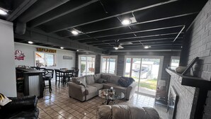 Ein modernes Wohnzimmer mit Ecksofa, Couchtisch und Kamin. Es gibt einen Essbereich mit Bar und Stühlen. Der Raum verfügt über große Fenster und einen Blick ins Freie.