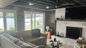 Ein Wohnzimmer mit einer Eckcouch, einem Glastisch, einem Kamin und Blick auf einen See.