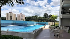 A swimming pool with a tiled deck, outdoor seating, and a view of surrounding buildings. - Bright Studio - GRU (Guarulhos)