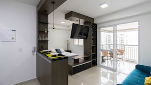 A modern apartment with a kitchen, a dining area, a living room with a blue sofa, and a balcony with outdoor furniture. - Bright Studio - GRU (Guarulhos)