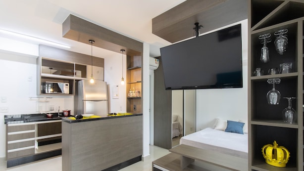 A modern kitchen with a central island, built-in microwave, and a flat-screen TV mounted above the island. - Bright Studio - GRU (Guarulhos)