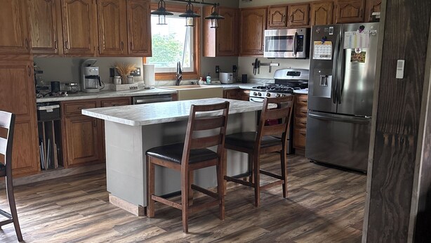 A kitchen with wooden cabinets, a central island with chairs, a stove, and a refrigerator. - Spacious Home that is close to EAA and Shopping. (Oshkosh)