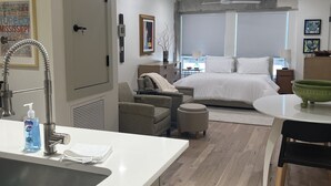 A modern hotel room with a kitchenette, a bed, a seating area, and a large window. - Easy walk to restaurants, coffee and ice cream shops, retail shopping, and more! (Tupelo)