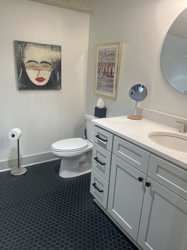 Een badkamer met toilet, wastafel met spiegel, een zakdoekendoos en een citaat in een lijst op de muur.