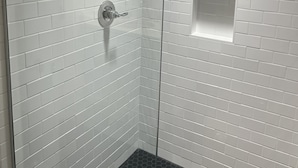 A shower with white tiled walls and a black tiled floor. - Easy walk to restaurants, coffee and ice cream shops, retail shopping, and more! (Tupelo)
