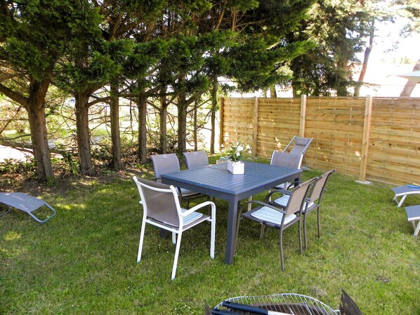 Eine Terrasse im Freien mit Tisch und Stühlen, umgeben von Bäumen und einem Holzzaun.
