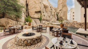 Eine Terrass mit Steintischen und -stühlen, einem Feuerkorb und einem Pool.