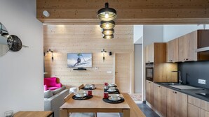 A modern kitchen with wooden cabinets, a dining table set for four, and a television mounted on the wall. - PERLE DE SAVOIE A402 (CHATEL)