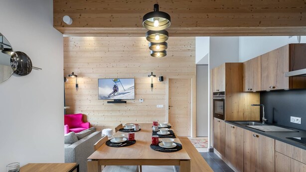 A modern kitchen with wooden cabinets, a dining table set for four, and a television mounted on the wall.