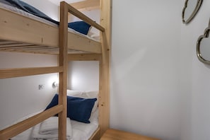 A bunk bed room with a wooden ladder, white walls, and a small wooden table.