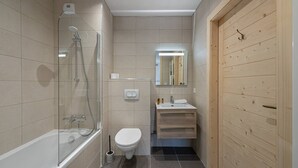 A modern bathroom with a glass-enclosed shower, a white toilet, a sink with a mirror above it, and wooden paneling on one wall. - PERLE DE SAVOIE A402 (CHATEL)