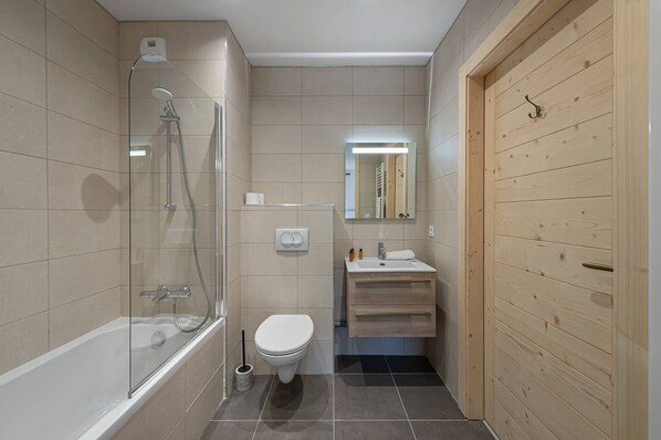 A modern bathroom with a glass-enclosed shower, a white toilet, a sink with a mirror above it, and wooden paneling on one wall.