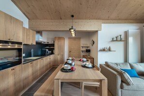 A modern kitchen with wooden cabinets, a dining table set with dishes, and a hanging light fixture.