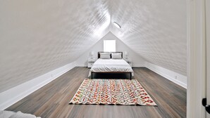 A bedroom with a sloped ceiling, a bed with a patterned bedspread, a nightstand, and a rug.