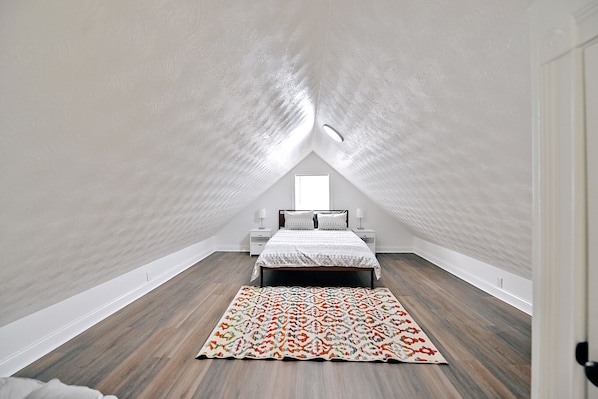 A bedroom with a sloped ceiling, a bed with a patterned bedspread, a nightstand, and a rug. - Urban Comfort & Cozy 4BR Near Downtown Indianapolis (Indianapolis)