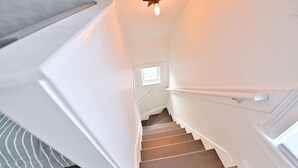 A staircase with white walls and a wooden handrail, leading to a small window at the top.