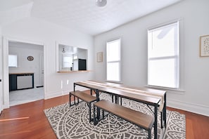 A dining area with a wooden table and benches, large windows, and a patterned rug. - Urban Comfort & Cozy 4BR Near Downtown Indianapolis (Indianapolis)