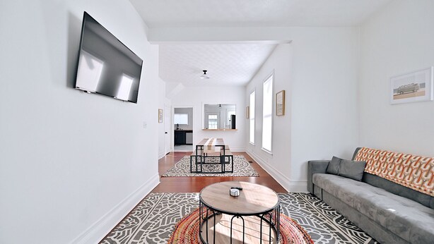 A spacious living area with a modern design, featuring a sofa, a coffee table, and a TV mounted on the wall.